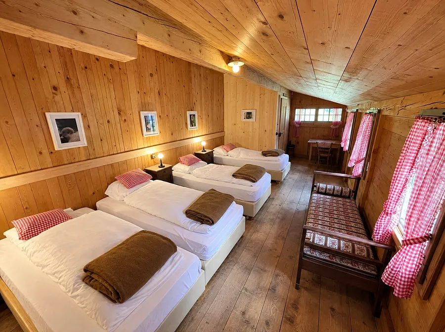 Langes Zimmer mit vier Betten und rot karierten Vorhängen
